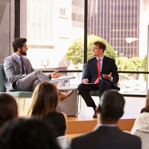 speaker-and-interviewer-talk-in-front-of-audience-PB95UA7